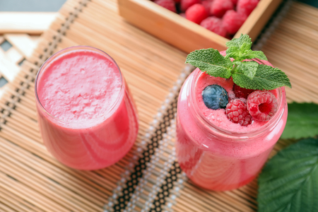 Glass and jar with tasty raspberry smoothie on tableの写真素材