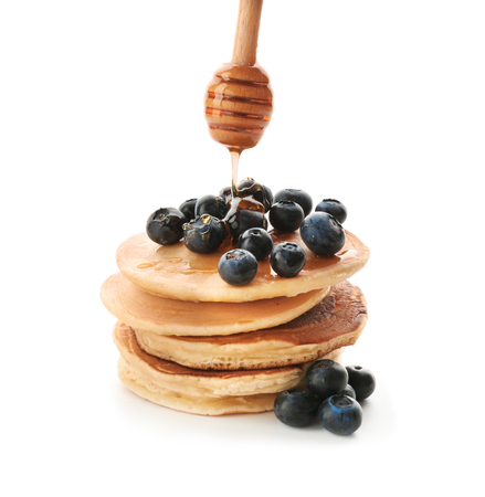 Pouring of honey onto delicious pancakes with berries on white backgroundの写真素材