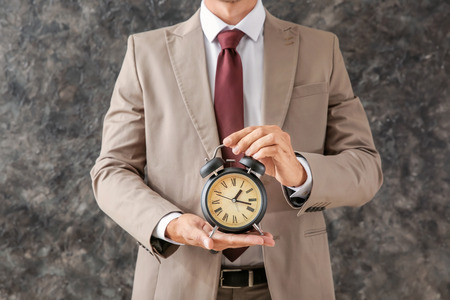 Businessman holding alarm clock on grey background. Time management conceptの写真素材