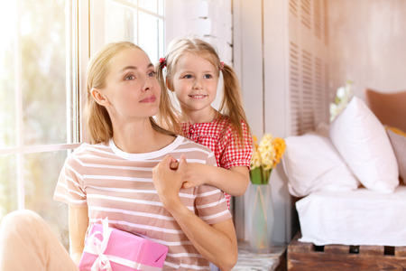 Portrait of cute little girl and her mother with gift box at homeの写真素材