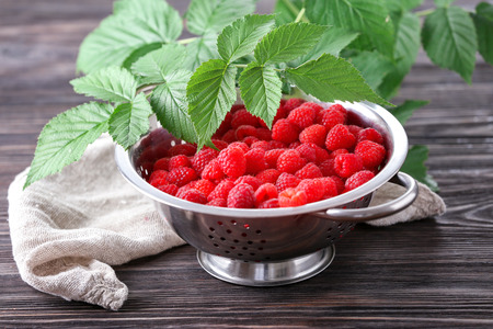 Colander with ripe raspberry on wooden table