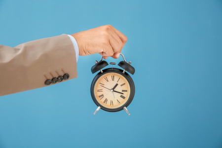 Businessman holding alarm clock on color background. Time management conceptの写真素材