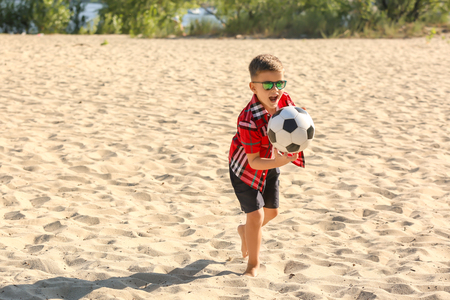 Little boy playing football on sand beachの写真素材