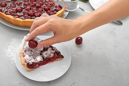 Woman decorating piece of sweet pie with ripe cherry in kitchenの写真素材