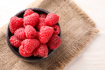 Bowl with sweet ripe raspberries on table