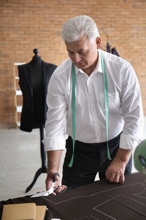 Mature tailor cutting fabric in atelierの写真素材