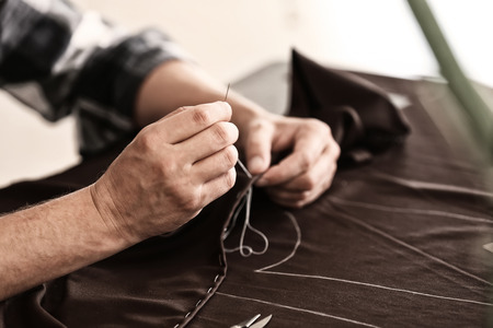 Young tailor sewing at table in atelier, closeupの写真素材