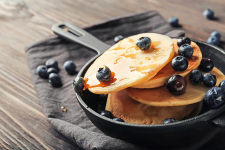 Frying pan with delicious pancakes and berries on wooden table, closeup