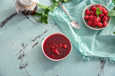 Bowls with sweet jam and fresh raspberries on table