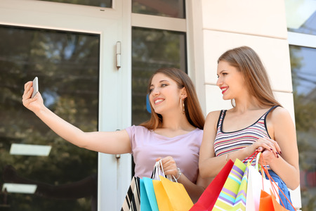 Young women with shopping bags taking selfie on city streetの写真素材