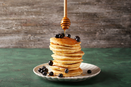 Pouring of honey onto delicious pancakes with berries on green tableの写真素材
