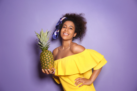 Beautiful African-American woman with pineapple on color backgroundの写真素材