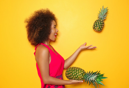 Beautiful African-American woman with pineapples on color background
