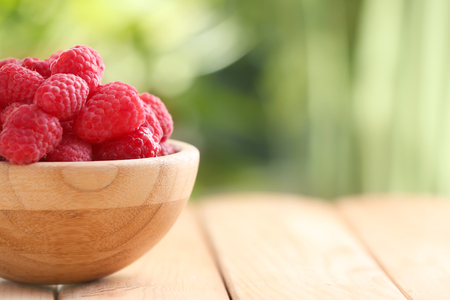 Wooden bowl with sweet ripe raspberries on table outdoorsの写真素材