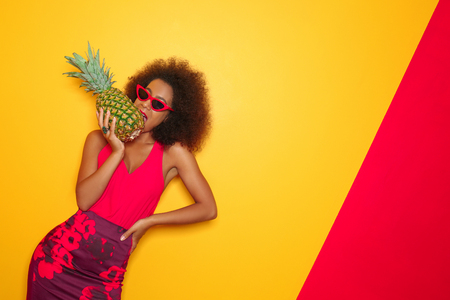 Beautiful African-American woman with pineapple on color backgroundの写真素材