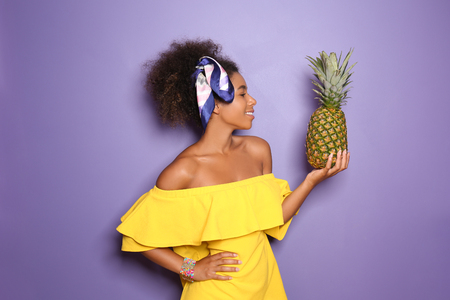 Beautiful African-American woman with pineapple on color backgroundの写真素材