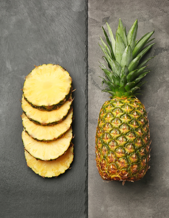 Slate plate with slices of ripe pineapple and whole fruit on grey backgroundの写真素材