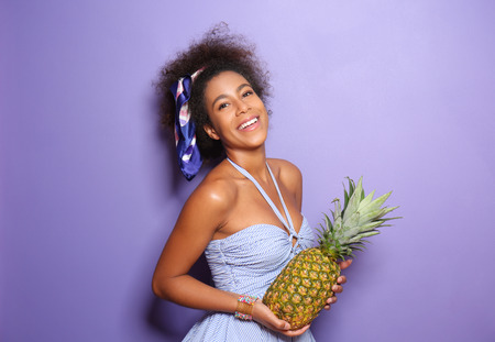 Beautiful African-American woman with pineapple on color background