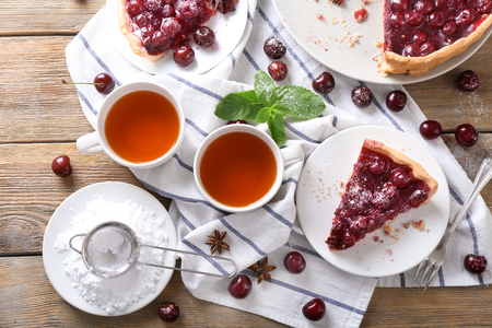 Delicious cherry pie with cups of aromatic tea on wooden tableの写真素材