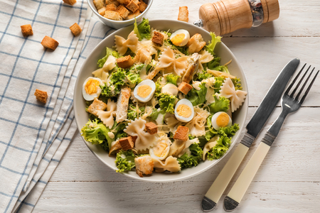 Tasty Caesar salad with pasta in bowl on wooden tableの写真素材