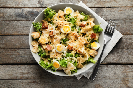 Tasty Caesar salad with pasta in bowl on wooden tableの写真素材