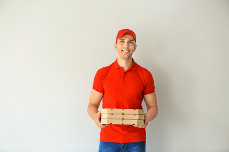 Young man with pizza boxes on light background. Food delivery service