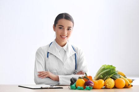 Female nutritionist sitting at table with clipboard and healthy products on white backgroundの写真素材