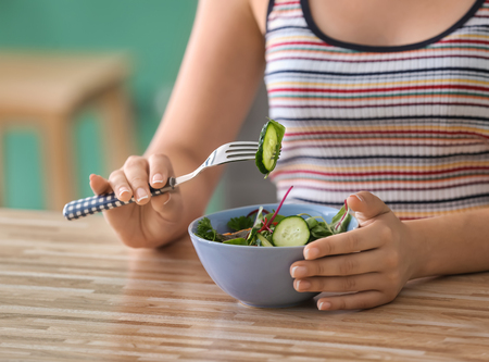 Young woman eating healthy salad with vegetables at homeの写真素材