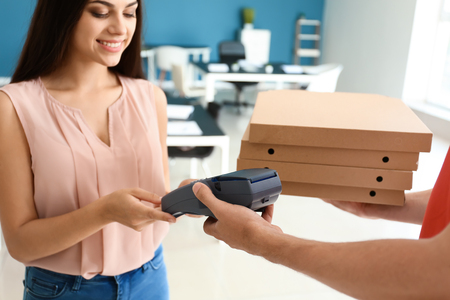 Young woman using bank terminal to pay for food delivery indoorsの写真素材