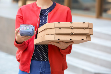 Young woman with pizza boxes and bank terminal outdoors. Food delivery serviceの写真素材