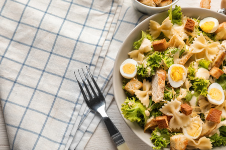 Tasty Caesar salad with pasta in bowl on wooden tableの写真素材