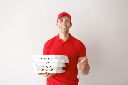 Young man with pizza boxes showing thumb-up gesture on light background. Food delivery serviceの写真素材