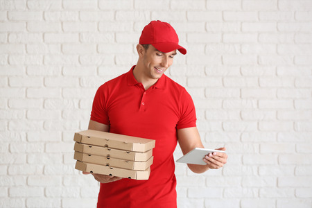 Young man with pizza boxes and tablet computer near white brick wall. Food delivery serviceの写真素材