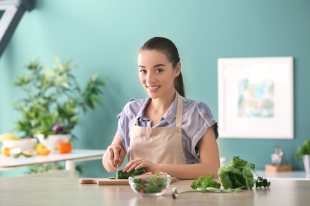 Young woman cutting vegetables for salad in kitchenの写真素材