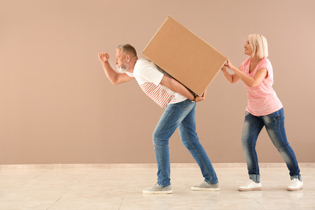 Mature couple with box near color wall indoors. Moving into new houseの写真素材