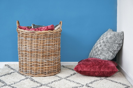 Soft pillows with wicker basket on carpet near color wall indoorsの写真素材