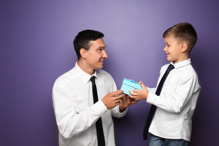 Little boy giving present to his father on color backgroundの写真素材