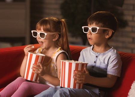 Cute children in 3d glasses watching movie on sofa in eveningの写真素材