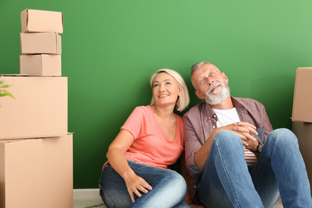 Mature couple sitting on floor near boxes indoors. Moving into new houseの写真素材