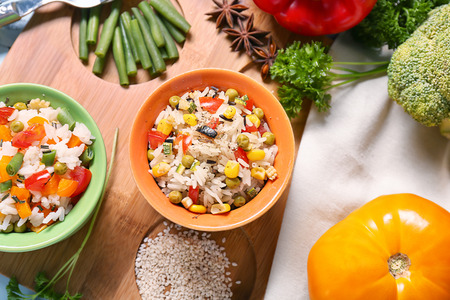Bowls with tasty boiled rice and vegetables on wooden boardの写真素材