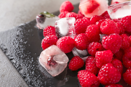 Fresh ripe raspberries with ice on slate plate, closeup