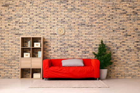 Interior of living room with stylish red sofa near brick wall