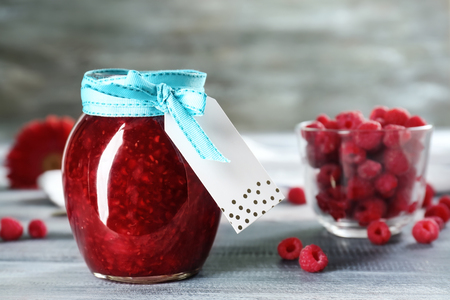 Glass jar with tasty raspberry jam on wooden table