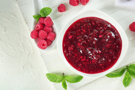 Bowl with tasty raspberry jam on white table