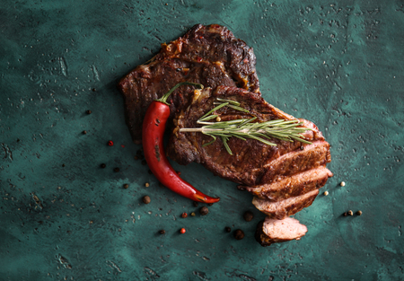 Tasty cut grilled meat with chili pepper, spices and herbs on green tableの写真素材