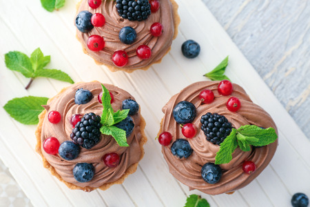 Tasty tartlets with chocolate cream and berries on white boardの写真素材