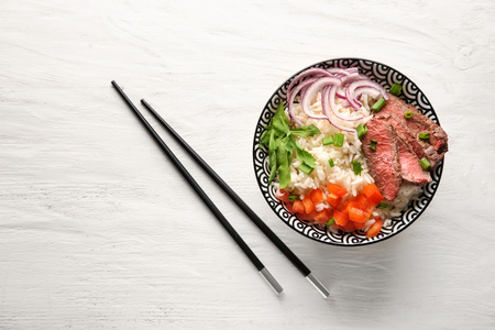 Delicious boiled rice with meat and vegetables in bowl on wooden tableの写真素材