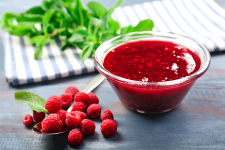 Bowl with tasty raspberry jam on wooden table