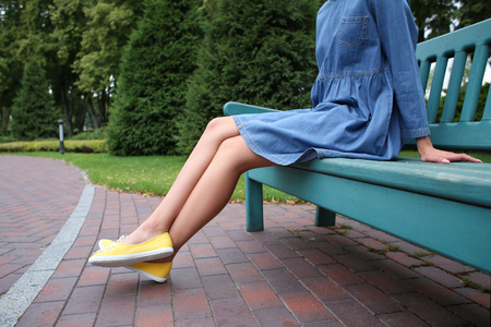 Young woman in gumshoes resting on bench outdoorsの写真素材
