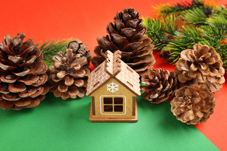 Christmas composition with wooden house and pine cones on color backgroundの写真素材